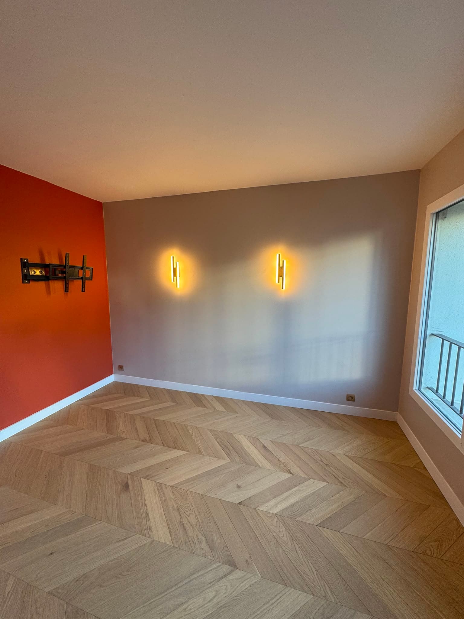 Mur accent orangé, appliques dorées et parquet chevron